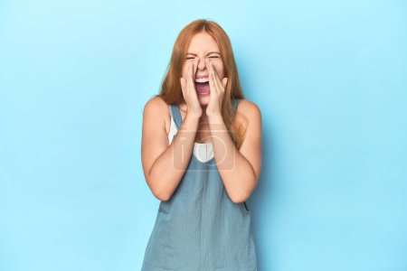 Photo for Redhead young woman on blue background shouting excited to front. - Royalty Free Image