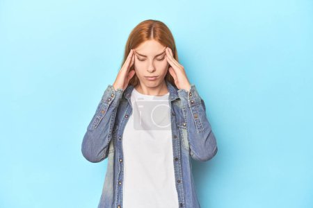 Photo for Redhead young woman on blue background touching temples and having headache. - Royalty Free Image