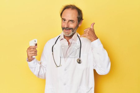 Foto de Doctor sosteniendo termómetro infrarrojo en el estudio mostrando un gesto de llamada de teléfono móvil con los dedos. - Imagen libre de derechos