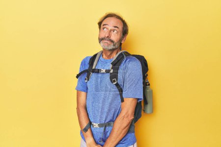 Téléchargez les photos : Randonneur d'âge moyen avec sac à dos en studio rêvant d'atteindre des objectifs et des buts - en image libre de droit