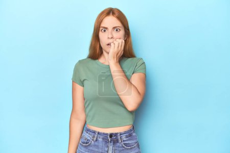 Photo for Redhead young woman on blue background biting fingernails, nervous and very anxious. - Royalty Free Image