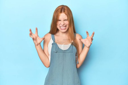 Photo for Redhead young woman on blue background screaming with rage. - Royalty Free Image