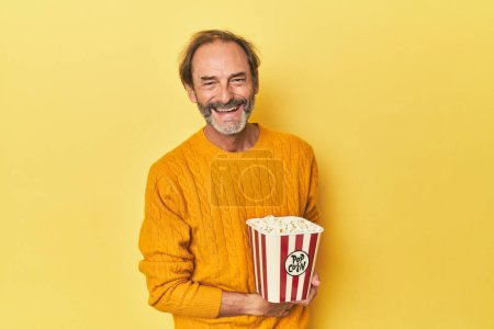 Téléchargez les photos : Homme appréciant pop-corn en studio jaune rire et s'amuser. - en image libre de droit