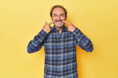 Téléchargez les photos : Blanc d'âge moyen homme en jaune studio sourit, les doigts pointant vers la bouche. - en image libre de droit