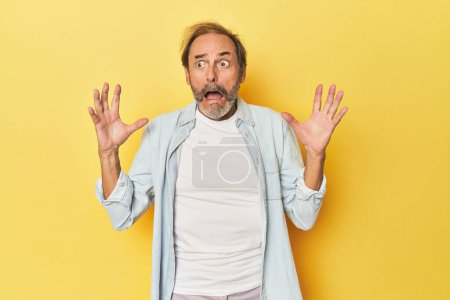 Photo for Caucasian middle-aged man in yellow studio screaming to the sky, looking up, frustrated. - Royalty Free Image