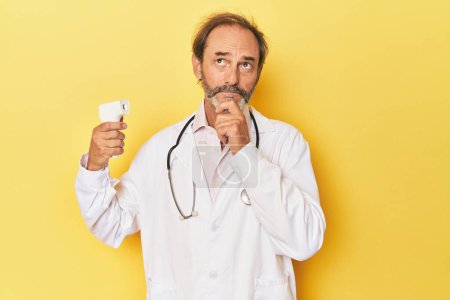 Foto de Doctor sosteniendo termómetro infrarrojo en estudio mirando de lado con expresión dudosa y escéptica. - Imagen libre de derechos