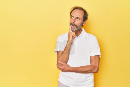 Téléchargez les photos : Homme d'âge moyen caucasien en studio jaune regardant latéralement avec une expression douteuse et sceptique. - en image libre de droit
