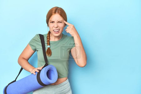 Photo for Redhead young woman holding yoga mat in studio showing a disappointment gesture with forefinger. - Royalty Free Image