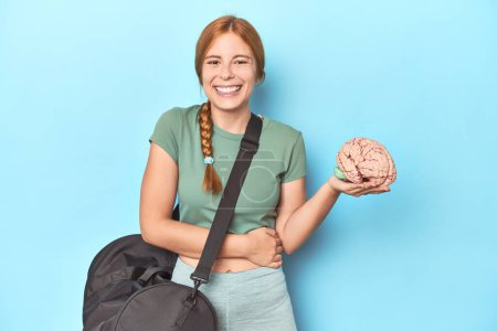Photo for Sporty redhead with brain model on blue background laughing and having fun. - Royalty Free Image