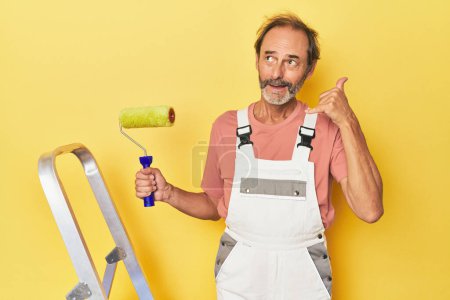 Téléchargez les photos : Homme peignant en toile de fond jaune en studio montrant un geste d'appel téléphonique mobile avec les doigts. - en image libre de droit
