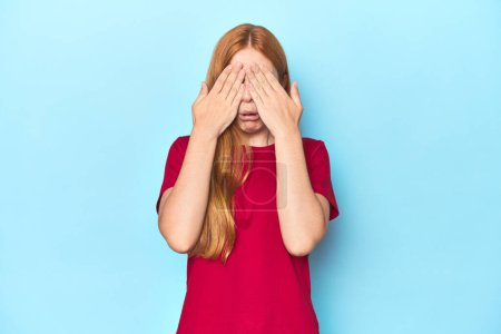 Photo for Redhead young woman on blue background afraid covering eyes with hands. - Royalty Free Image