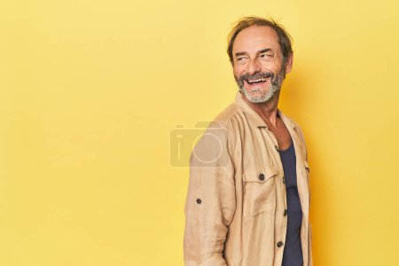 Foto de Caucásico hombre de mediana edad en estudio amarillo mira a un lado sonriente, alegre y agradable. - Imagen libre de derechos