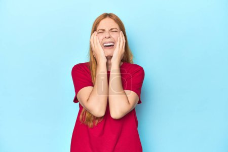 Photo for Redhead young woman on blue background crying, unhappy with something, agony and confusion concept. - Royalty Free Image