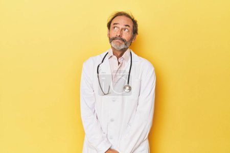 Photo for Doctor with stethoscope in yellow studio dreaming of achieving goals and purposes - Royalty Free Image