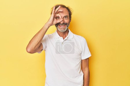 Téléchargez les photos : Caucasien d'âge moyen l'homme en jaune studio excité garder ok geste sur oeil. - en image libre de droit