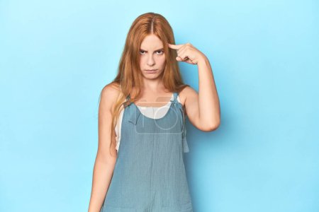 Photo for Redhead young woman on blue background pointing temple with finger, thinking, focused on a task. - Royalty Free Image