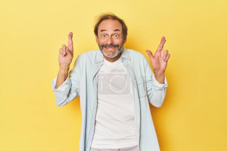 Téléchargez les photos : Blanc homme d'âge moyen en studio jaune croisant les doigts pour avoir de la chance - en image libre de droit