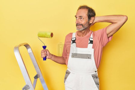 Téléchargez les photos : Homme peignant en toile de fond jaune en studio touchant l'arrière de la tête, pensant et faisant un choix. - en image libre de droit