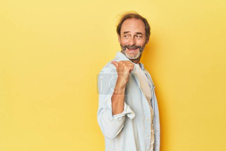 Foto de Caucásico hombre de mediana edad en amarillo puntos de estudio con el dedo pulgar de distancia, riendo y sin preocupaciones. - Imagen libre de derechos