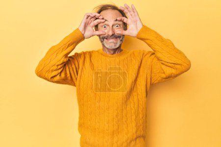Téléchargez les photos : Homme d'âge moyen caucasien en studio jaune gardant les yeux ouverts pour trouver une opportunité de succès. - en image libre de droit