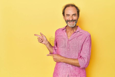 Photo for Caucasian middle-aged man in yellow studio excited pointing with forefingers away. - Royalty Free Image
