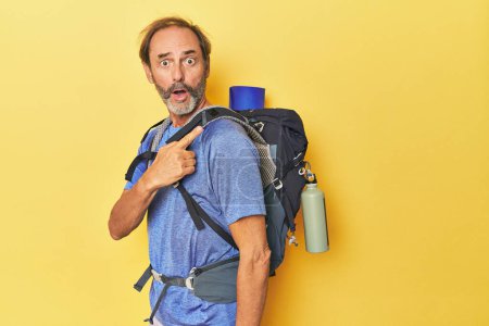 Photo for Middle-aged hiker with backpack in studio pointing to the side - Royalty Free Image