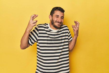 Téléchargez les photos : Jeune homme hispanique sur fond jaune croisant les doigts pour avoir de la chance - en image libre de droit
