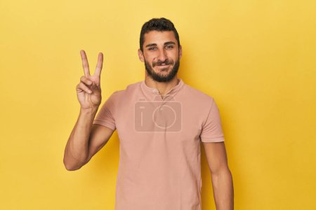 Foto de Joven hispano sobre fondo amarillo alegre y despreocupado mostrando un símbolo de paz con los dedos. - Imagen libre de derechos