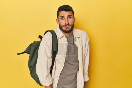 Téléchargez les photos : Jeune homme hispanique avec sac à dos de voyage haussant les épaules et les yeux ouverts confus. - en image libre de droit