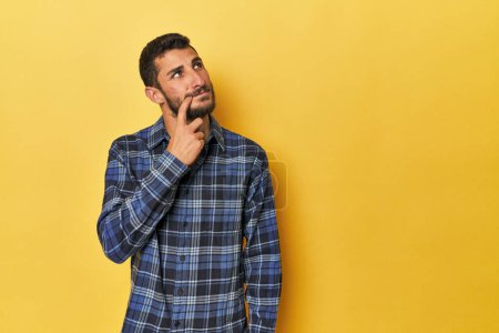 Photo for Young Hispanic man on yellow background looking sideways with doubtful and skeptical expression. - Royalty Free Image