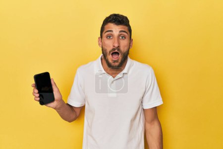 Photo for Young Hispanic man shows phone screen screaming very angry and aggressive. - Royalty Free Image