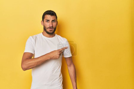 Téléchargez les photos : Jeune homme hispanique sur fond jaune pointant vers le côté - en image libre de droit
