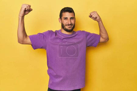 Téléchargez les photos : Jeune homme hispanique sur fond jaune montrant un geste de force avec des bras, symbole du pouvoir féminin - en image libre de droit