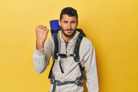 Téléchargez les photos : Jeune homme hispanique prêt pour la randonnée montrant poing à caméra, expression faciale agressive. - en image libre de droit