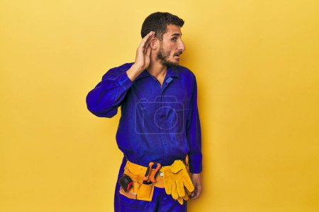 Photo for Young Hispanic man in a blue jumpsuit Young Hispanic man in a blue jumpsuittrying to listening a gossip. - Royalty Free Image