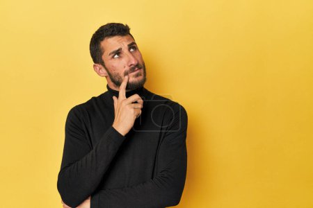 Téléchargez les photos : Jeune homme hispanique sur fond jaune regardant de côté avec une expression douteuse et sceptique. - en image libre de droit