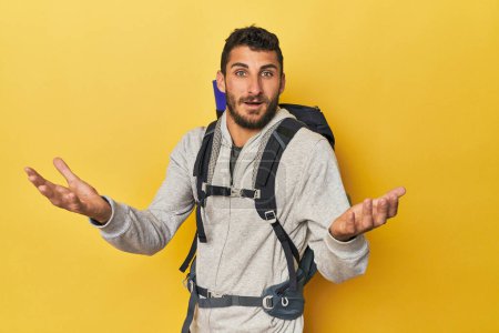 Photo for Young Hispanic man ready for hiking receiving a pleasant surprise, excited and raising hands. - Royalty Free Image