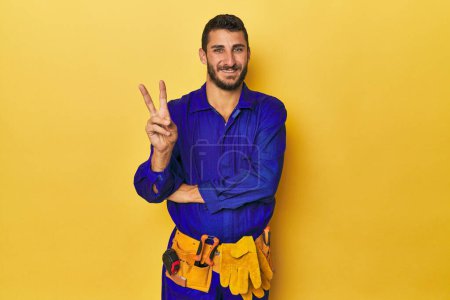 Photo for Young Hispanic man in a blue jumpsuit Young Hispanic man in a blue jumpsuitshowing number two with fingers. - Royalty Free Image