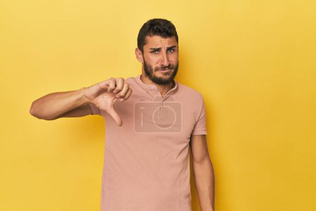Téléchargez les photos : Jeune homme hispanique sur fond jaune montrant pouce baissé, concept de déception. - en image libre de droit