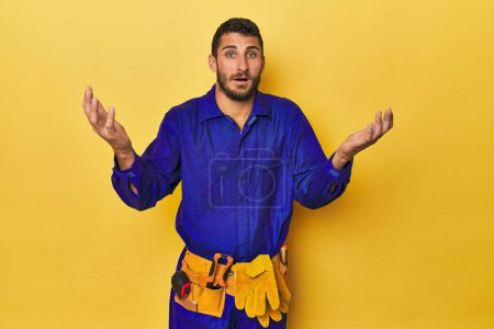 Photo for Young Hispanic man in a blue jumpsuit Young Hispanic man in a blue jumpsuitreceiving a pleasant surprise, excited and raising hands. - Royalty Free Image