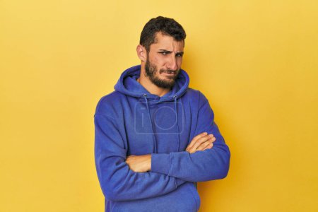Photo for Young Hispanic man on yellow background suspicious, uncertain, examining you. - Royalty Free Image