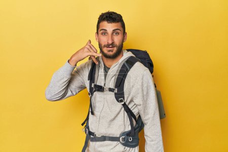 Téléchargez les photos : Jeune homme hispanique prêt pour la randonnée montrant un geste d'appel téléphonique mobile avec les doigts. - en image libre de droit