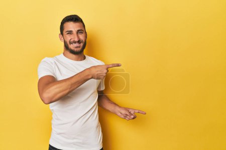 Téléchargez les photos : Jeune homme hispanique sur fond jaune pointant les index vers un espace de copie, exprimant excitation et désir. - en image libre de droit