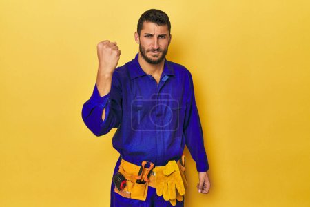 Photo for Young Hispanic man in a blue jumpsuit Young Hispanic man in a blue jumpsuitshowing fist to camera, aggressive facial expression. - Royalty Free Image