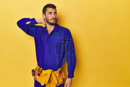Photo for Young Hispanic man in a blue jumpsuit Young Hispanic man in a blue jumpsuittouching back of head, thinking and making a choice. - Royalty Free Image