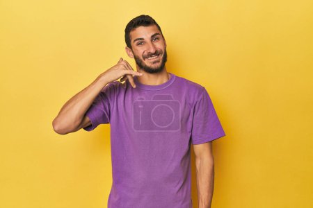 Téléchargez les photos : Jeune homme hispanique sur fond jaune montrant un geste d'appel téléphonique mobile avec les doigts. - en image libre de droit