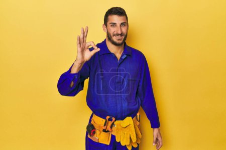 Photo for Young Hispanic man in a blue jumpsuit Young Hispanic man in a blue jumpsuitcheerful and confident showing ok gesture. - Royalty Free Image