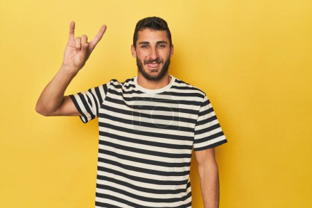 Téléchargez les photos : Jeune homme hispanique sur fond jaune montrant un geste de cornes comme concept de révolution. - en image libre de droit