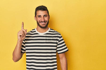 Téléchargez les photos : Jeune homme hispanique sur fond jaune montrant numéro un avec doigt. - en image libre de droit