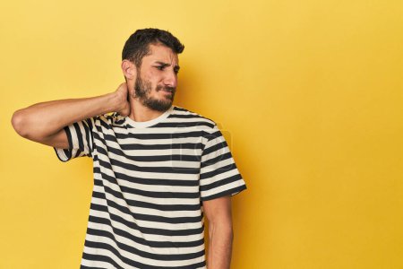 Téléchargez les photos : Jeune homme hispanique sur fond jaune touchant l'arrière de la tête, pensant et faisant un choix. - en image libre de droit